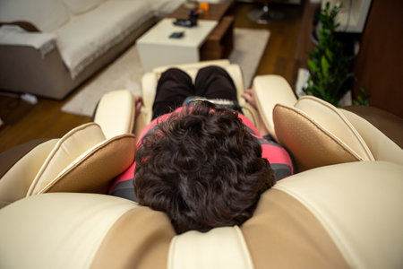 A senior woman lies on a massage chair in her apartment. She really adores massaging herself in this massage chair and enjoys it. Focus on head to senior women.の写真素材