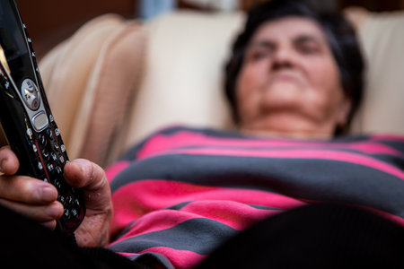 Selective focus on the remote control from the massage chair in the hand of a senior woman. A senior woman with short black hair is sitting in a massage chair.の写真素材