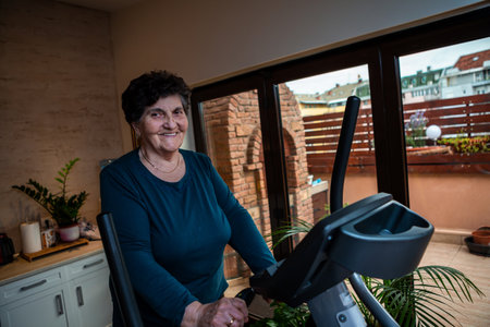 An older senior woman with black short hair is at home exercising on a training machine.の写真素材
