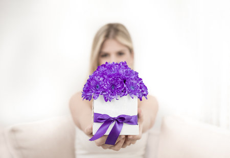 A young blonde is holding a bouquet of purple chrysanthemum flowers in a decorative box. The focus is on flowers.の写真素材