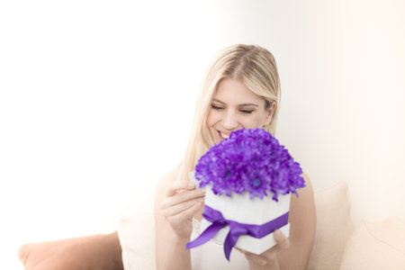 The young blonde holds a bouquet of flowers in her hands in a decorative box she received from a man she loves. She laughs and is very happy.の写真素材