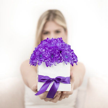A young blonde is holding a bouquet of purple chrysanthemum flowers in a decorative box. The focus is on flowers.の写真素材