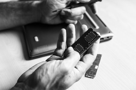 A human hand with a computer memory frame. He wants to install it in the laptop computer on the desk. Black and whiteの写真素材