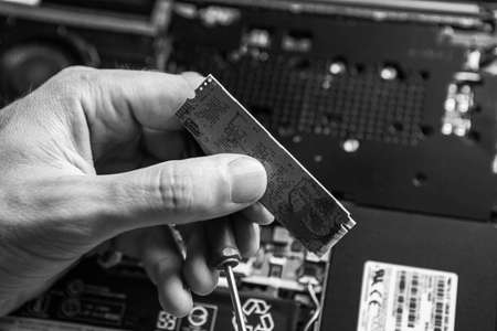 The service technician holds a new ssd drive in his hands, which he wants to put in the laptop, and he hopes that after that it will work. Black and White.の写真素材