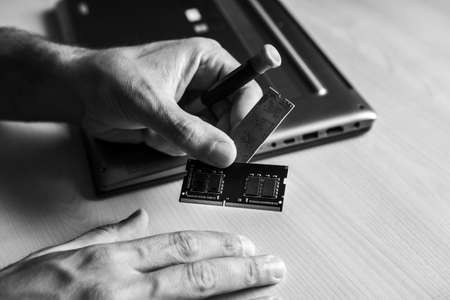 A human hand with a computer memory frame. He wants to install it in the laptop computer on the desk. Black and whiteの写真素材