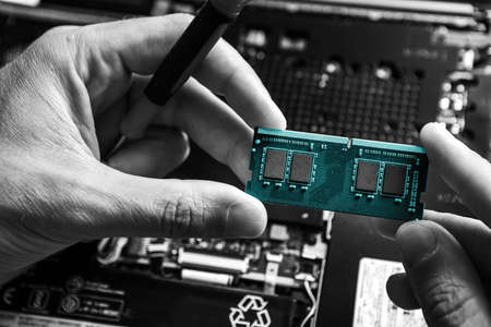 The service technician holds a new blue RAM in his hands, which he wants to put in the laptop, and he hopes that after that it will work. Black and white.の写真素材