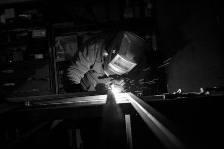 An adult male works in an old workshop. He holds a welding machine in his hand and welds the metal...