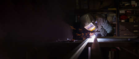 An adult male works in an old workshop. He holds a welding machine in his hand and welds the metal...
