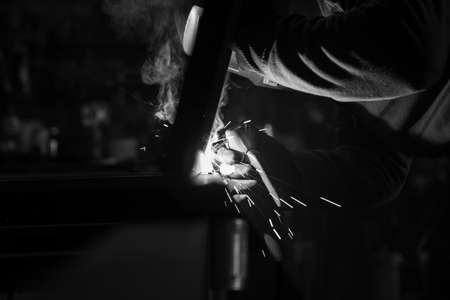 Close-up of a place where a welder welds two pipes. It is located in the workshop and the smoke...