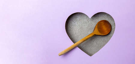 An old wooden cooking spoon is in a gray heart-shaped cavity. All around is purple. Copy Space. Love. Cooking. Food. Tradition.の写真素材