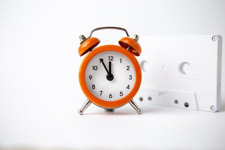 Old analog orange clock on a white background. The clock shows the time from five minutes to twelve...