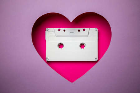 The white audio music cassette is located in a pink heart-shaped cavity. All around is purple. Copy Space. Love. Music. Old. Nostalgia.の写真素材