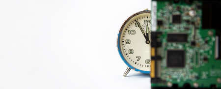 Old analog blue clock on a white background. The clock shows the time from five minutes to twelve o'clock, and in front is a printed circuit board, made of some electronics. Copy Space. Clock. Time.の写真素材