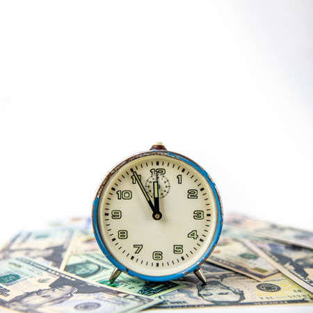An old blue ruined analog clock that shows five minutes to twelve o'clock. The watch is on US dollar bills. Concept time and money. Copy space.の写真素材