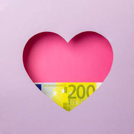 The two hundred euro banknote is in a pink heart on a purple background. Minimal concept money, love.の写真素材