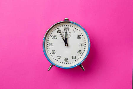 Old retro analog blue alarm clock on a pink background. The clock starts from five minutes to twelve o'clock.の写真素材