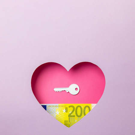 The key to the door and the two hundred euro banknote are in a pink heart on a purple background. Minimal concept of money, love and real estate. Copy space.の写真素材