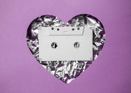 Heart shape on a pink background and in the heart a white music cassette and aluminum background. Concept of love and music.の写真素材