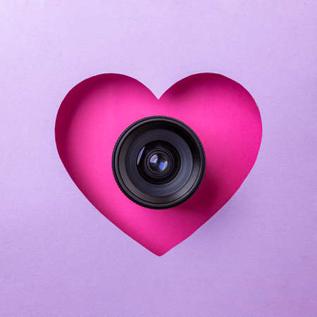 Pink heart on a purple background. At the heart is a camera lens. Concept of love, photography and video.の写真素材