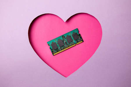 Pink heart shape on a purple background. At the heart are a memory frame for a computer and laptop. Minimal concept love computers.の写真素材