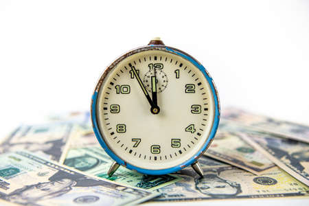 An old blue ruined analog clock that shows five minutes to twelve o'clock. The watch is on US dollar bills. Concept time and money.の写真素材
