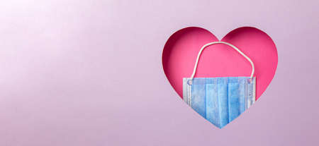 The medical blue mask is in a pink heart on a purple background. Minimal concept of love and medicine. Copy space.の写真素材