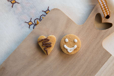 Top view of two cookies located on a wooden kitchen board. One cookie is heart-shaped and the other is smiley-shaped.の写真素材