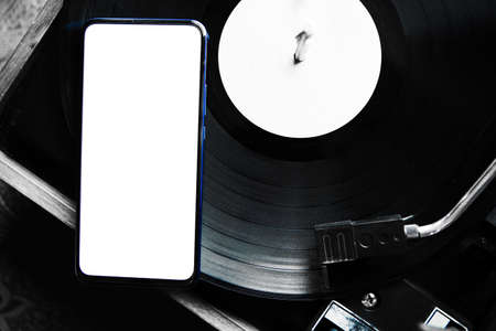 The new modern smartphone is on the music record on the turntable. The phone has a white screen. Music. Application. Copy space.の写真素材