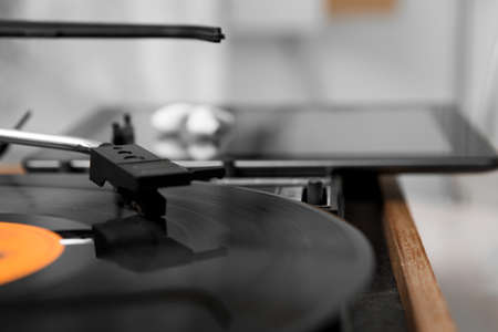 Selective focus on the head of a gramophone moving on a music record. behind it is a tablet computer and white wireless headphones on it.の写真素材