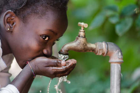 Beautiful African Child Drinking from a Tap (Water Scarcity Symbol). Young African girl drinking clean water from a tap. Water pouring from a tap in the streets of the African city Bamako, Mali.