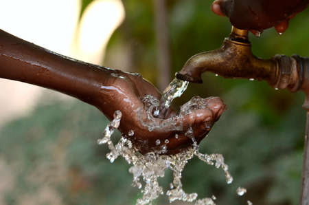 Happy African child holding her hand under clean fresh water - symbol for life and water scarcity in...