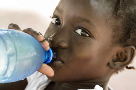 Poverty Symbol: African Black Girl Drinking Heathy Fresh Water. Poverty Symbol in Mali: African Black Girl Drinking Heathy Fresh Water from a bottle.の写真素材