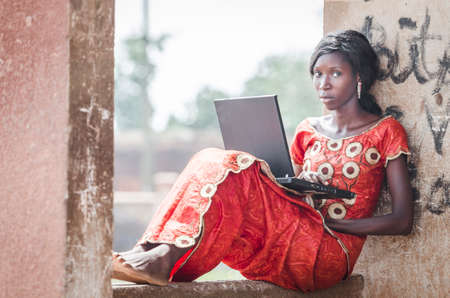 Young girl sitting on stone building and using laptop computer outdoors