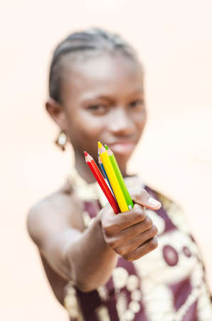 Young girl holding pencils in hand and looking at camera on beige backgroundの写真素材
