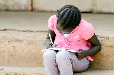 Young girl sitting on stone surface and writing on paper with penの写真素材