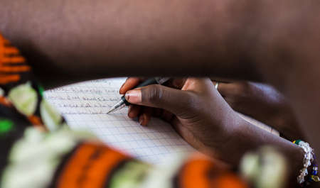 Close up view on female african hands writing on paper with blurred foreground