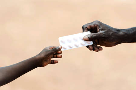 Adult african hand giving medicine to african child hand on beige backgroundの写真素材