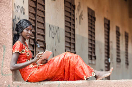 Young girl sitting on stone building and using tablet computer outdoorsの写真素材