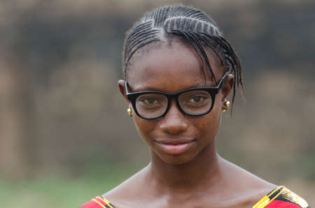 Young african girl in eyeglasses looking at camera outdoors with blurred backgroundの写真素材