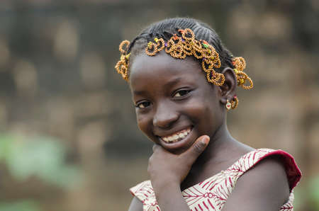 Young african girl with traditional accessories in hair looking at cameraの写真素材