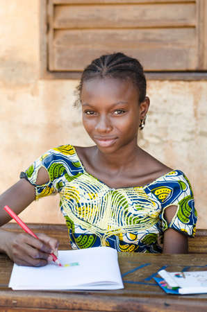 Young girl sitting at table and writing on paper with color pencilの写真素材