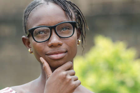 Young african girl in eyeglasses thinking outdoors with blurred backgroundの写真素材