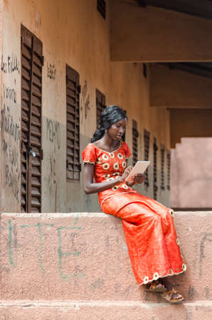Young girl sitting on stone building and using tablet computer outdoorsの写真素材