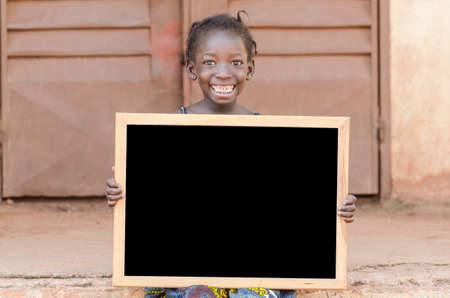 Girl sitting and holding signboard and looking at camera in front of buildingの写真素材