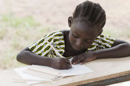 Young girl sitting at table and writing on paper with pencilの写真素材