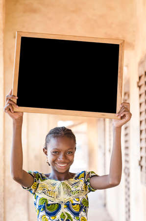 Girl sitting and holding signboard and looking at camera in front of buildingの写真素材