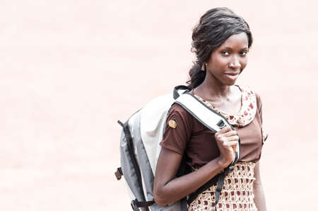 Young woman with backpack looking at camera on blurred beige backgroundの写真素材