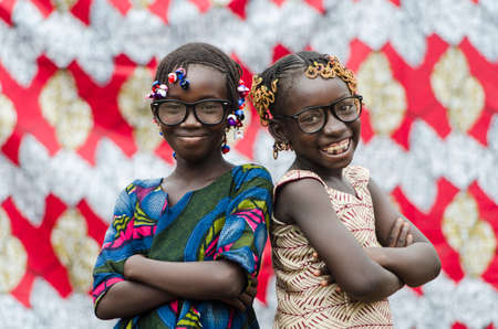 Young african girls with traditional accessories in hair standing back to back looking at cameraの写真素材