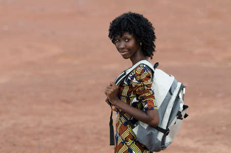 Young woman with backpack looking at camera on blurred beige backgroundの写真素材
