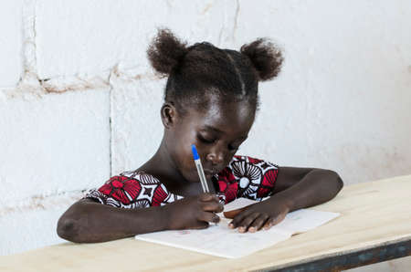 Young girl sitting at table and writing on paper with color penの写真素材